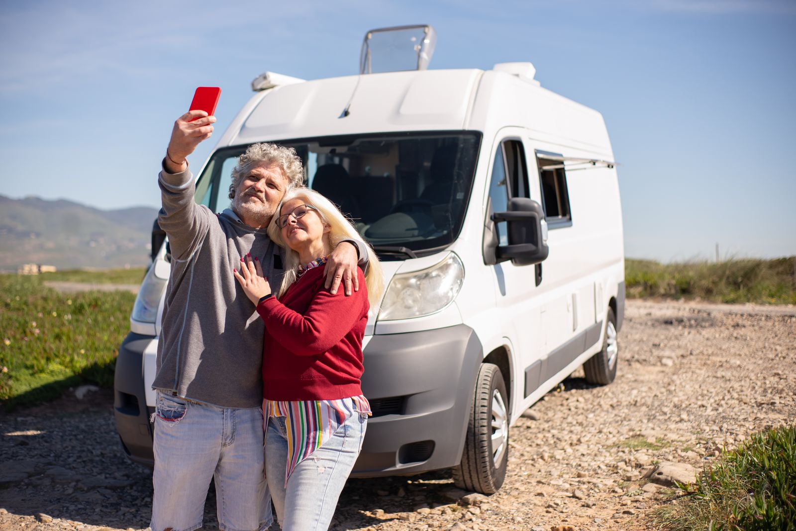 Senior couple taking a selfie beside their RV on a sunny trip