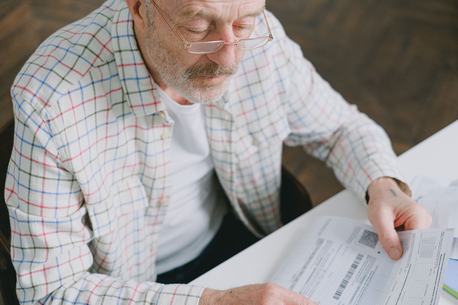 Retiree working through plan paperwork alone at his kitchen table before a review