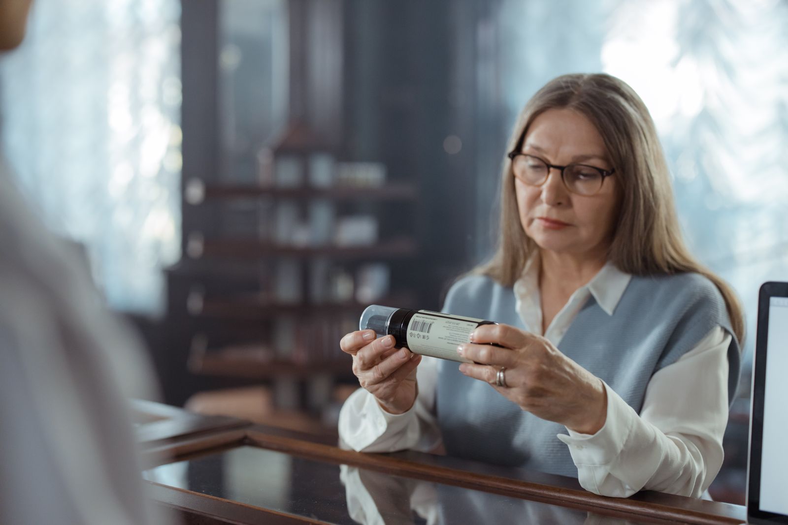 Senior woman reading a medicine bottle at a pharmacy counter